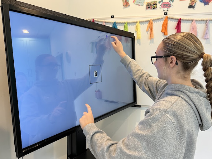 A patient points to a letter target on an interactive touchscreen during a vision therapy exercise at Navigation Eye Care