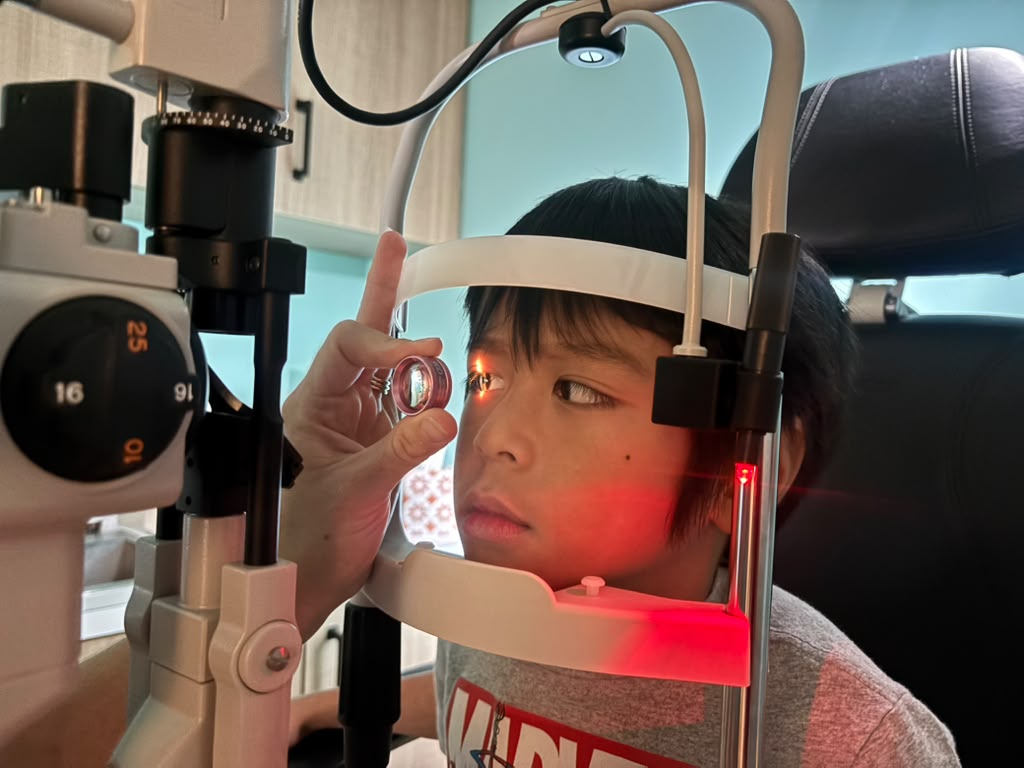 A young patient undergoes a slit lamp eye exam at Navigation Eye Care, with a hand-held lens positioned in front of his eye.