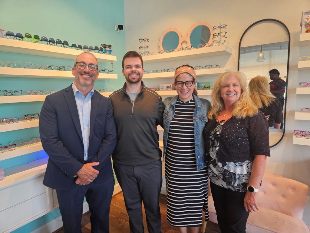 Four smiling adults pose together in front of eyewear displays at Navigation Eye Care.