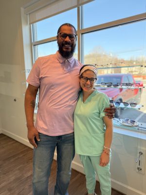 Happy patient with Navigation Eye Care team member holding new glasses in Chesapeake VA